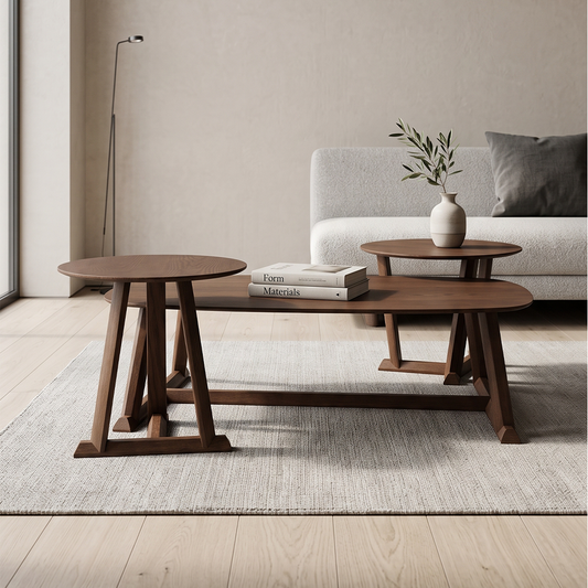 Three nested oval wooden coffee tables in a warm medium brown finish, styled in a minimalist living room with a light gray sofa, a white vase, and a neutral rug.