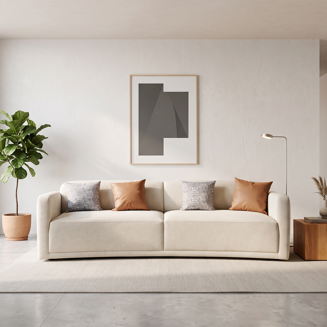 A modern beige fabric sofa with three decorative throw pillows, styled in a minimalist living room setting with a potted plant, a floor lamp, and framed wall art.