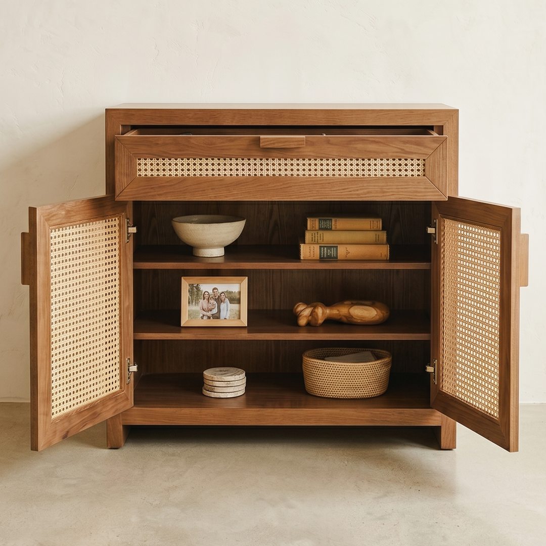 A mid-century modern wooden cabinet with open doors and cane panel inserts, styled with books, a bowl, a picture frame, and decorative objects inside, set against a neutral textured wall and concrete floor.